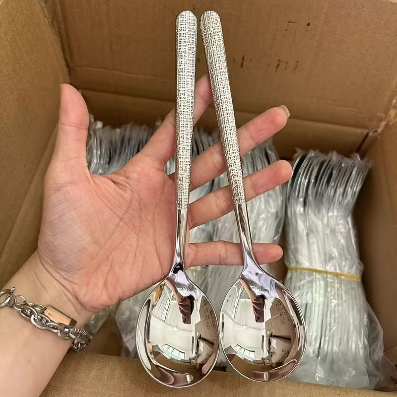 Two silver spoons held by a hand in front of a cardboard box with more spoons inside.
