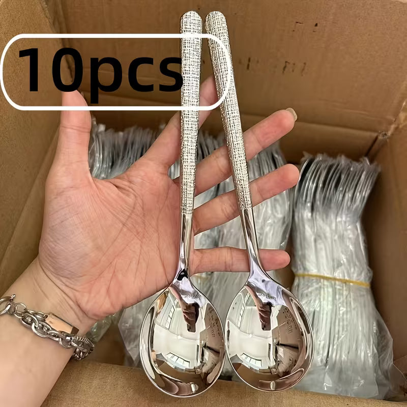 Two silver spoons held by a hand with a cardboard box in the background containing more spoons.