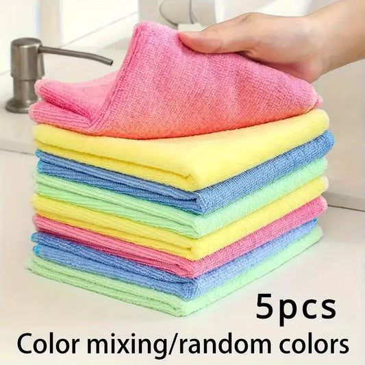 Stack of colorful microfiber cloths with a hand holding one, placed on a kitchen counter.