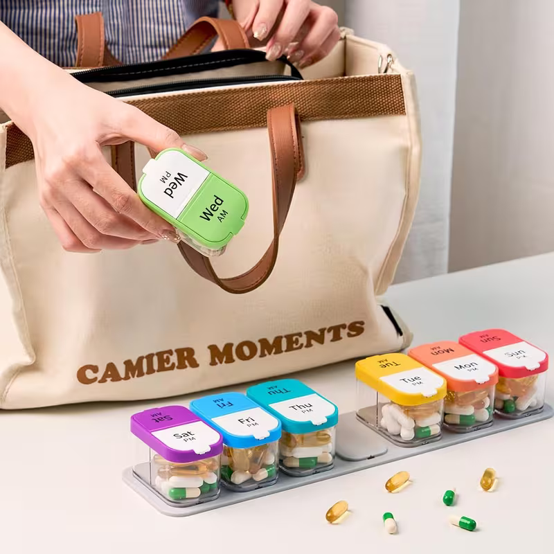 Person holding a pill organizer with labeled containers next to a 'Camier Moments' bag.