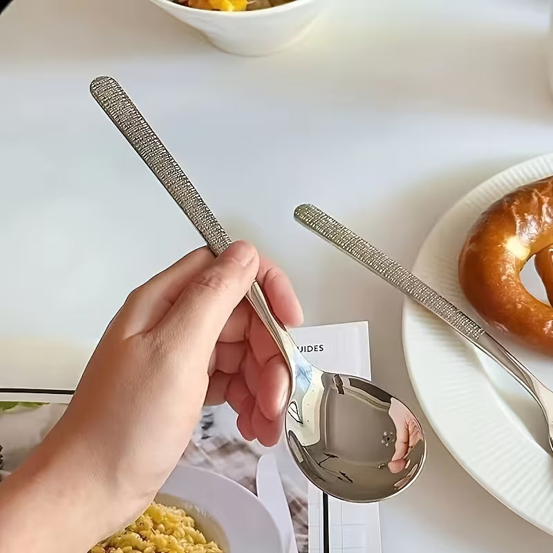 Person holding a decorative spoon with a white plate and food in the background