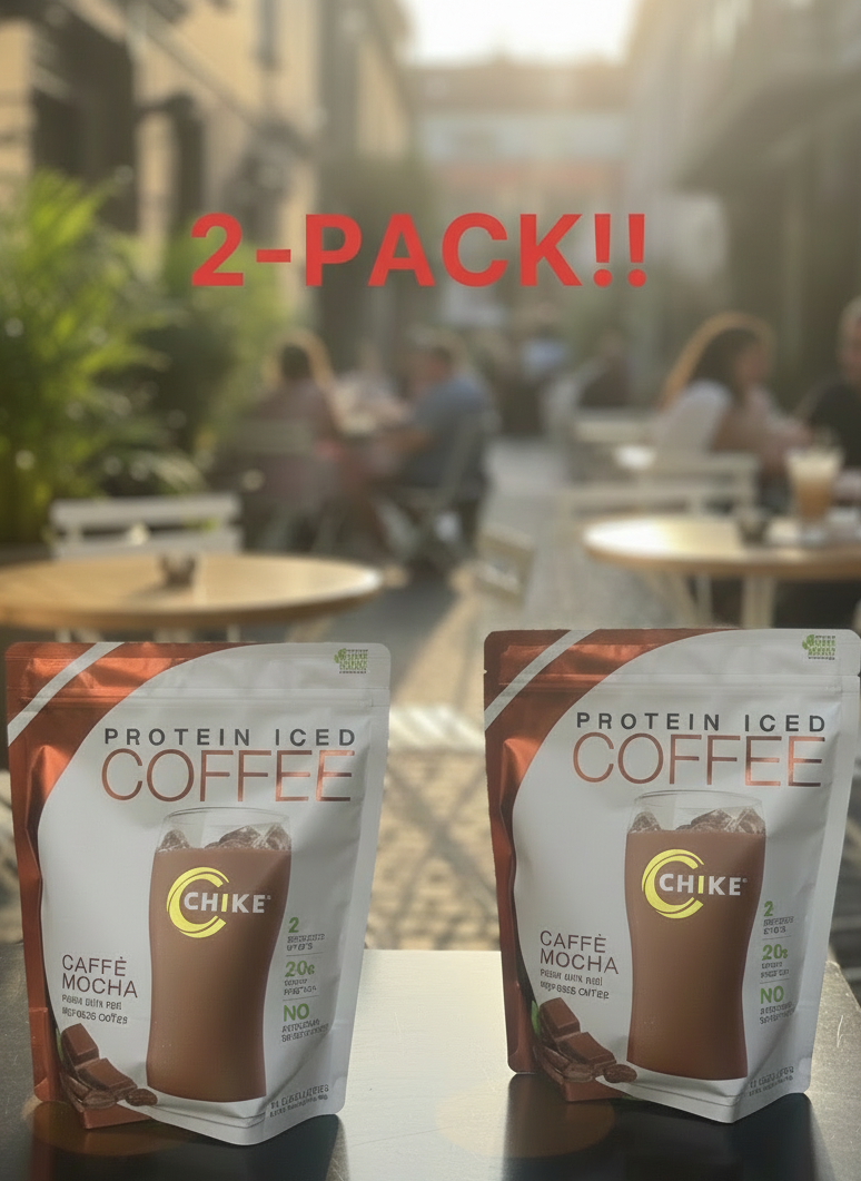 Two packages of Chike Protein Iced Coffee on a table with a blurred outdoor cafe background.