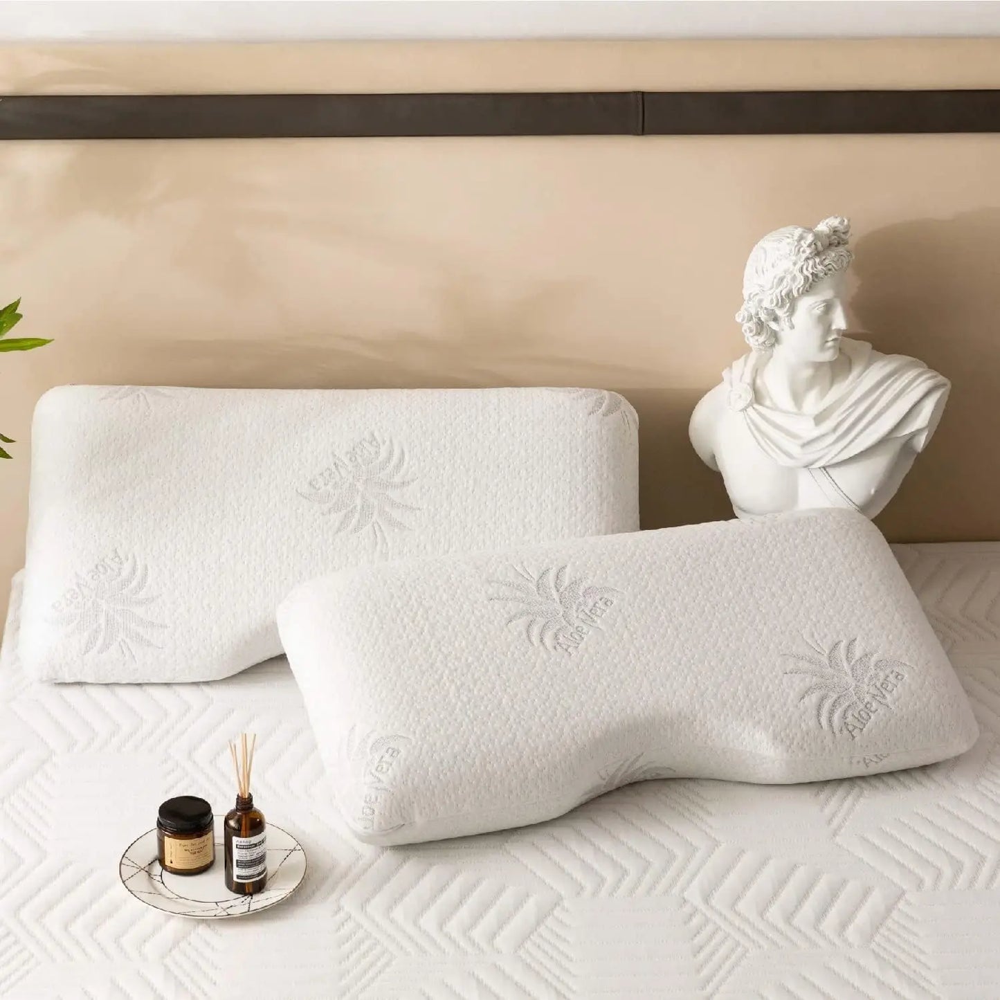 Two white pillows on a bed with a decorative bust and small items in the background.