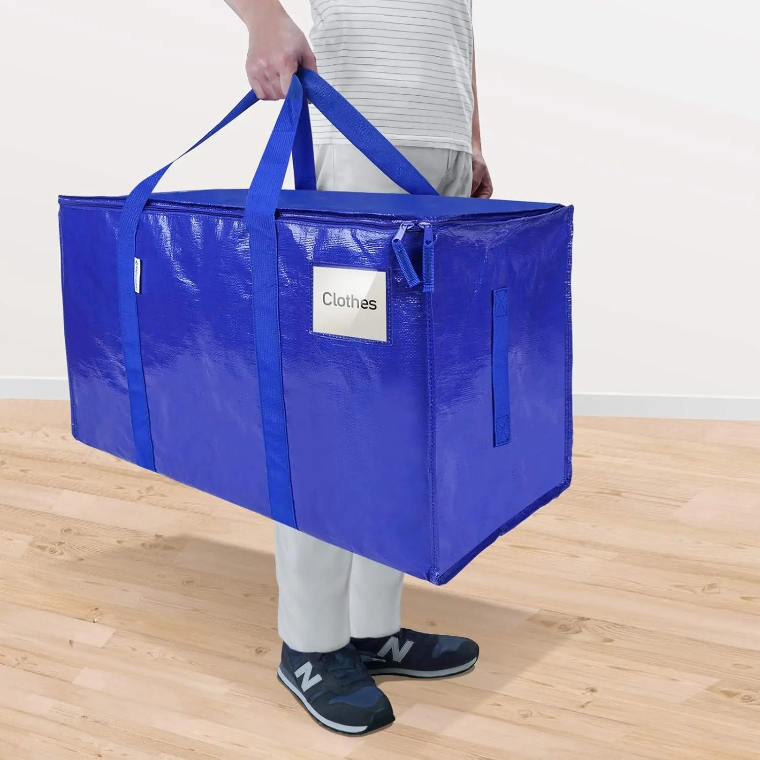 Person holding a large blue storage bag labeled 'Clothes' on a wooden floor.