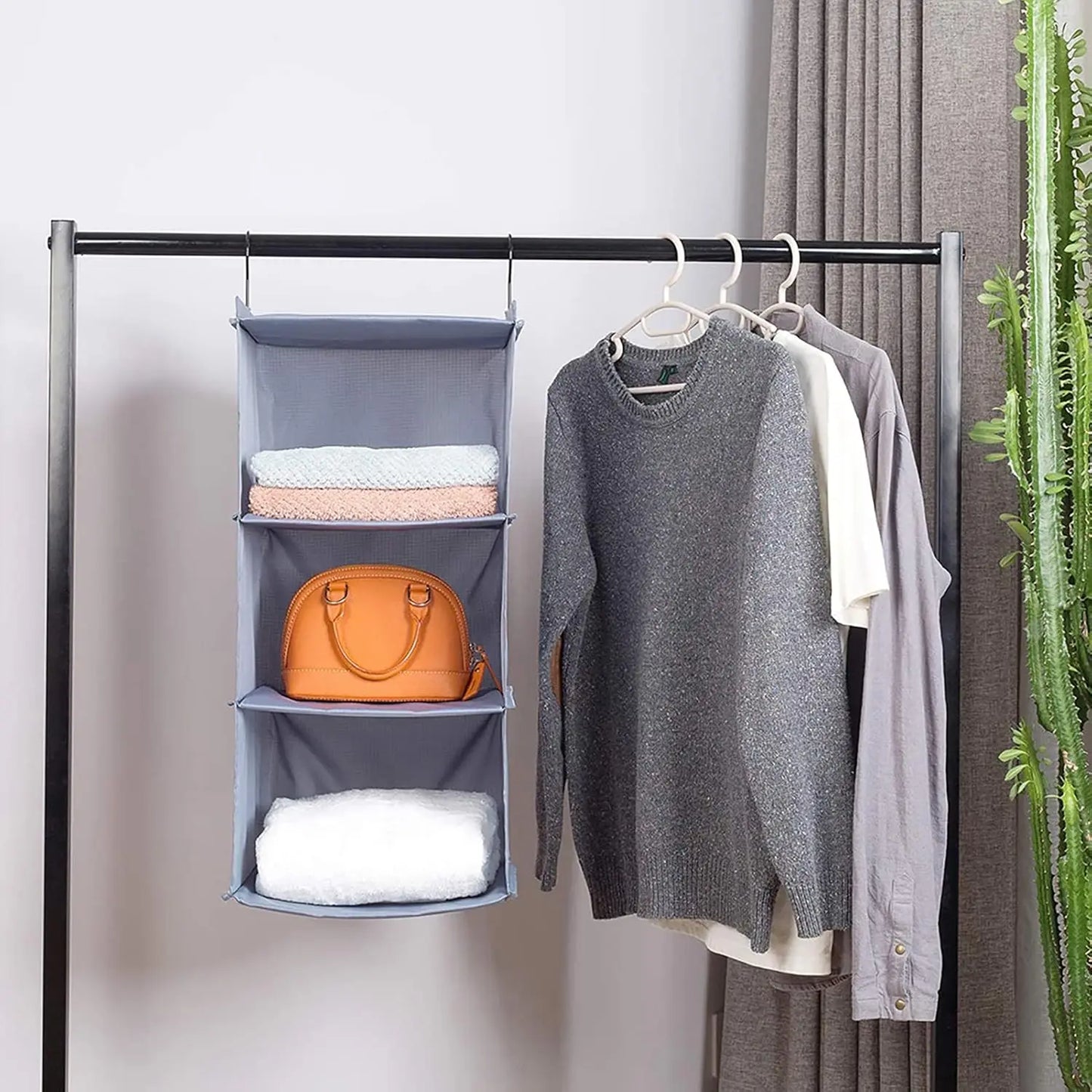 Hanging organizer with folded clothes and a handbag next to a clothing rack with hanging garments.