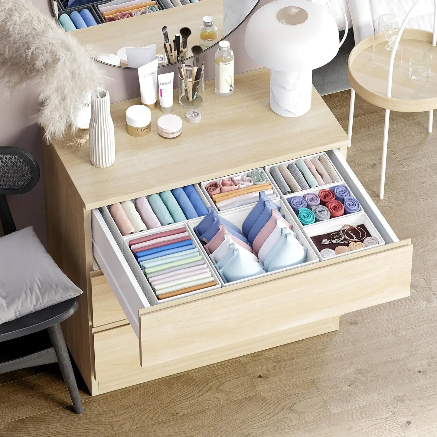 Wooden dresser with open drawer containing colorful folded clothes, surrounded by a mirror and chair.