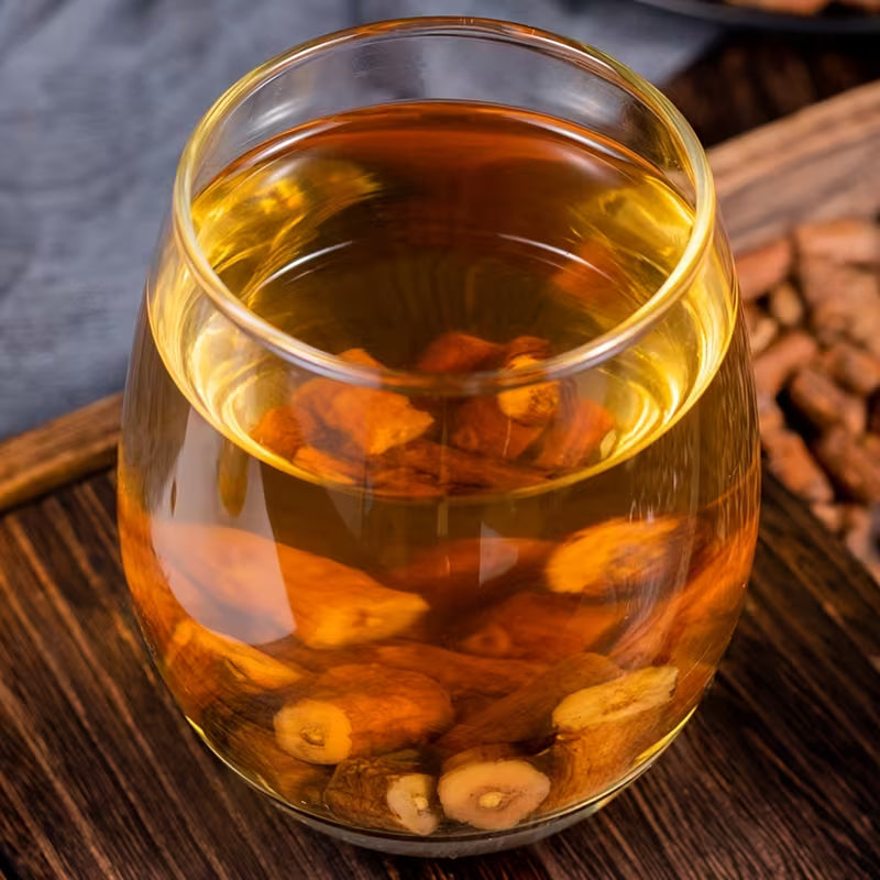 Glass of herbal tea with floating herbs on a wooden surface