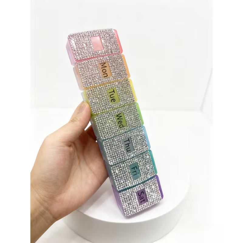 Multicolored weekly pill organizer with rhinestone embellishments held by a hand on a white background