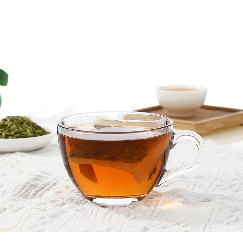 Clear glass mug filled with tea on a white surface with green leaves and a wooden tray in the background.