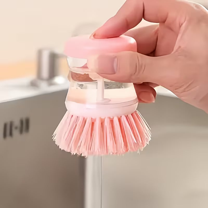 Pink dish scrubber held by a hand with a blurred kitchen background